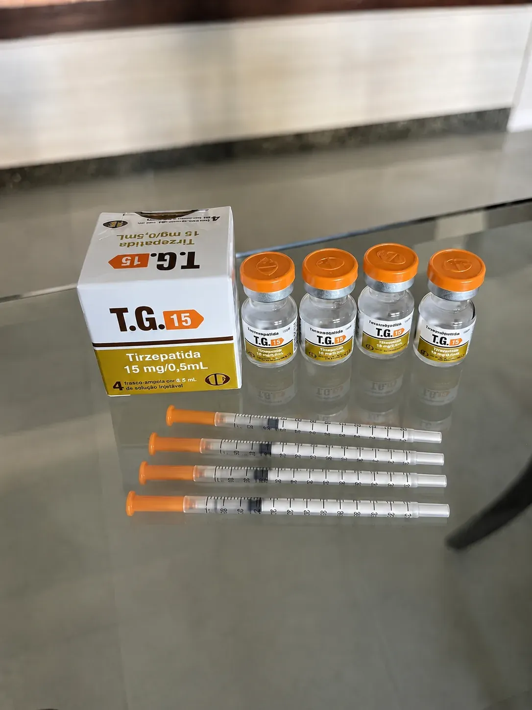 Kit da TG 15 Tirzepatida com caixa, quatro frascos e quatro seringas sobre superfície refletiva