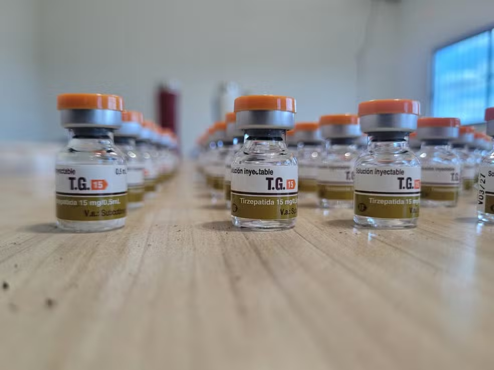 Frascos de T.G. 15 Tirzepatida 15 mg/0,5 mL com tampa laranja alinhados sobre bancada de madeira